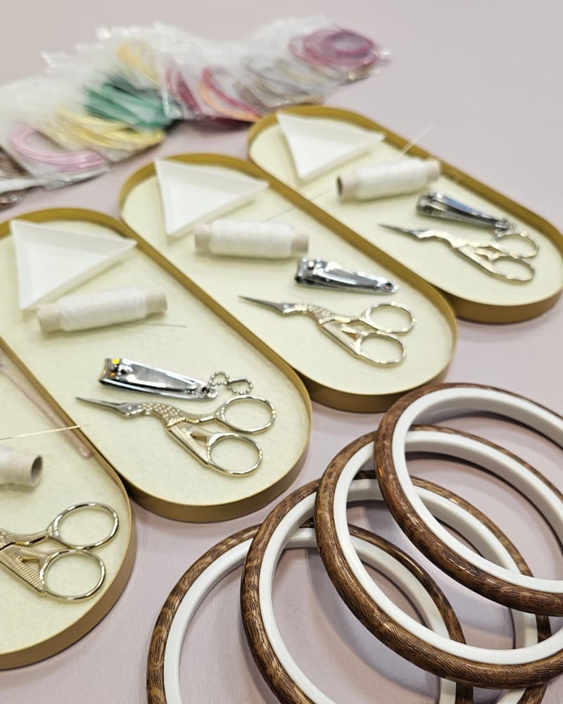 Bead embroidery tools laid out on a studio table — stork scissors, thread spools, needles, and wooden rings